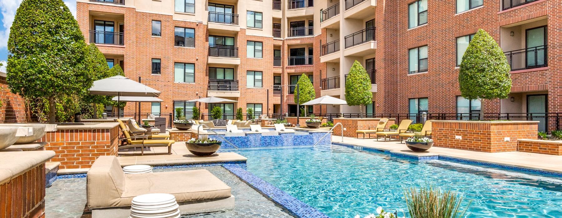 a pool with chairs and tables by it and buildings around it